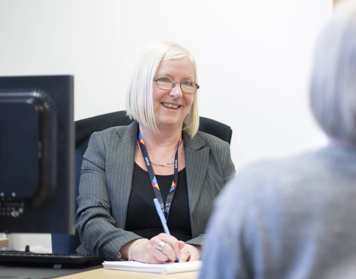 Staff member in a professional meeting at Glasgow Kelvin College, smiling and taking notes at her desk. Staff member in a professional meeting at Glasgow Kelvin College, smiling and taking notes at her desk.